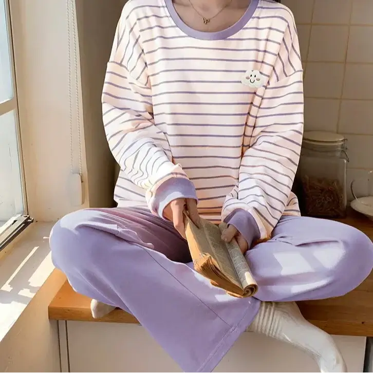 Person in a relaxed fit striped shirt and cozy pants reads by sunny window. Pairing offers breathable comfort with organic cotton.