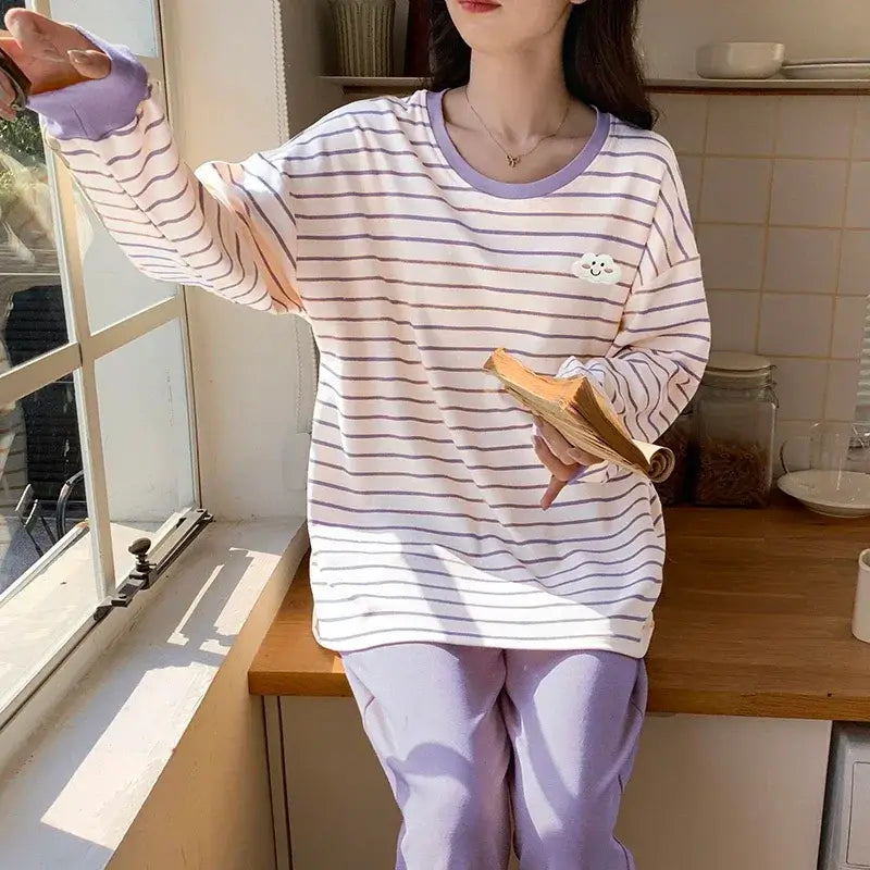 Person wearing a striped purple and white pajama set, sitting by a window with a book, in a cozy kitchen setting.