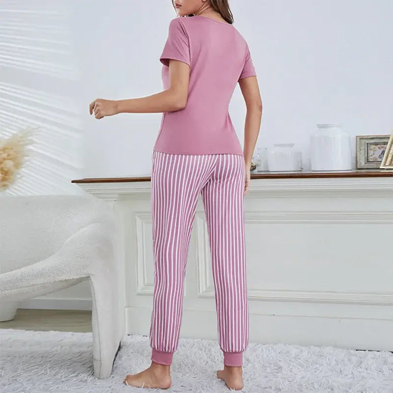 Woman wearing organic cotton sleepwear in relaxed fit, pink top with striped pants. Breathable material for comfort and style.