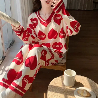 Woman wearing red heart-patterned loungewear set, holding a book, sitting beside a table with tea. Cozy and casual home setting.